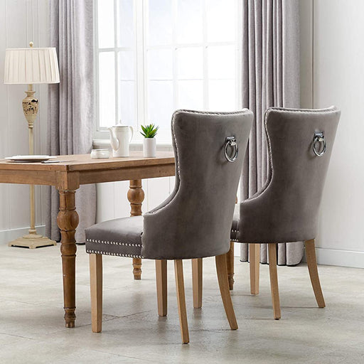 Back view of gray velvet tufted dining chairs with silver ring pulls at rustic table